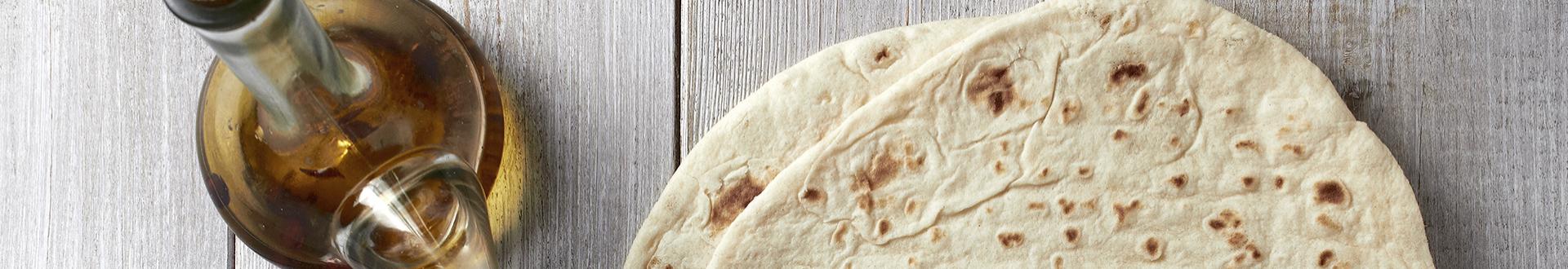 Piadina su tavola di legno accanto a bottiglia di olio d'oliva.
