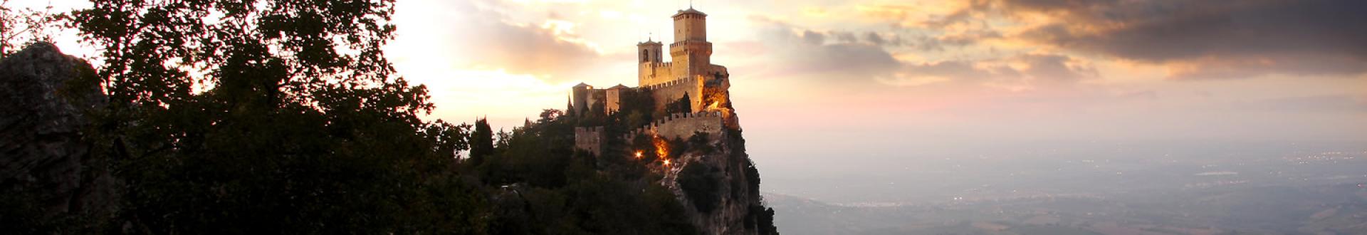 Castello su una collina al tramonto, con cielo nuvoloso e paesaggio sottostante.