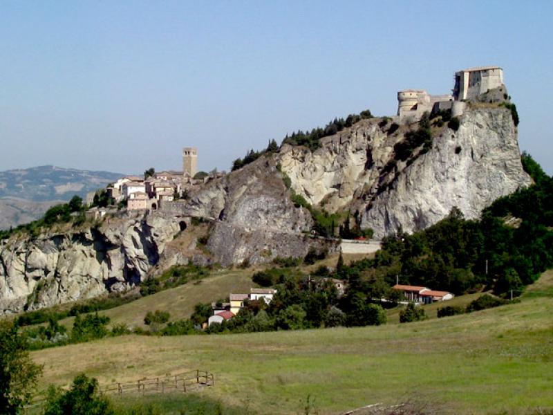 Paesaggio collinare con un borgo e una fortezza su una rupe.