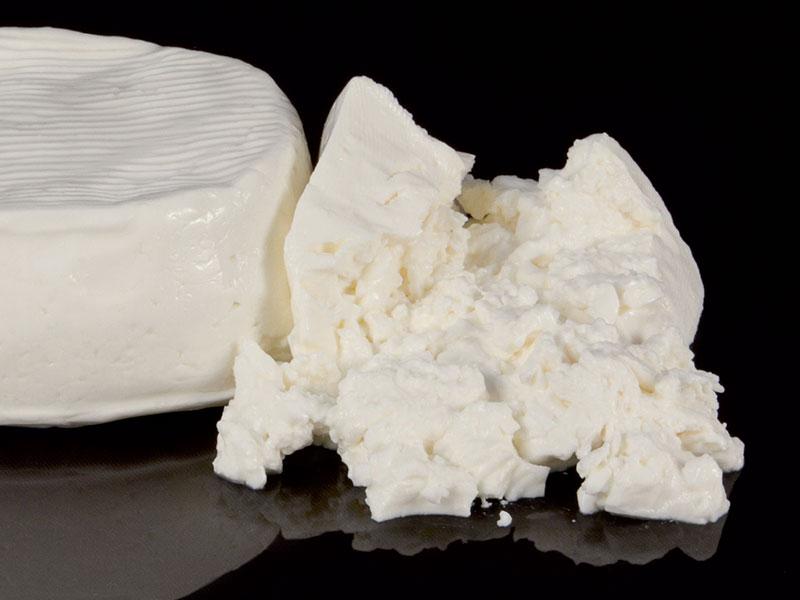 Formaggio fresco bianco, consistenza cremosa e friabile, su sfondo nero.